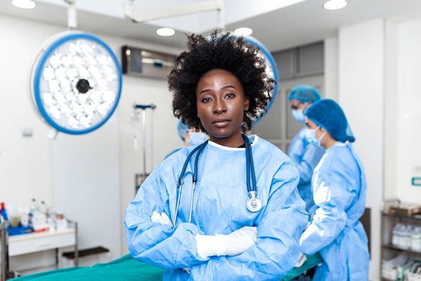 Egy afro-amerikai női sebész portréja, amint a műtőben áll, készen arra, hogy egy betegen dolgozzon. Női orvosi dolgozó sebészeti egyenruhában a műtőben. - Fotó, kép