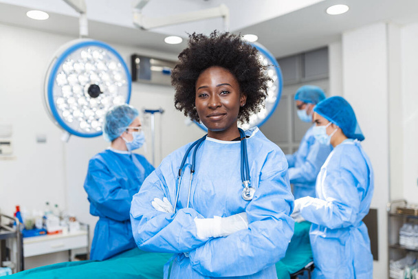 Portret Afroamerykanki w masce ochronnej przygotowującej się do operacji. Chirurg i jego asystent na niewyraźnym tle - Zdjęcie, obraz