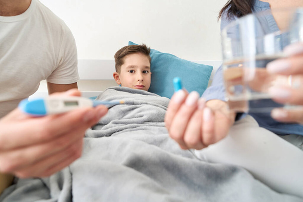 Добрі батьки піклуються про хворого хлопчика, приймають його температуру і дають йому ліки
 - Фото, зображення