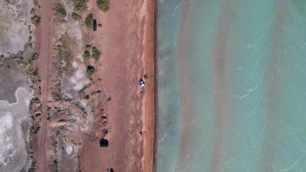 A beach with blue water color and sandy waves. Top view from a drone of vacationing people, tents and cars. Brown sand of Lake Balkhash. Blue sky. Bushes and several trees grow. Family vacation by sea - Filmati, video