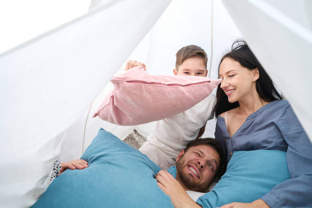 Mom and son jokingly threw pillows at dad, small family is comfortable in a hut - Fotó, kép