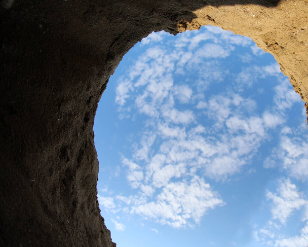 vista incomum de dentro de um buraco cavado na areia a partir do qual você pode ver o céu azul e nuvens - Foto, Imagem