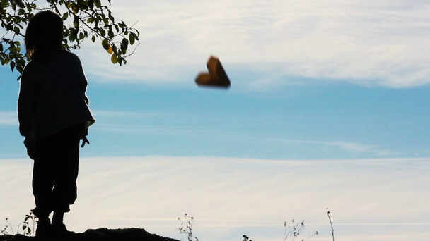 紙飛行機で遊ぶ少年のシルエット。孤独な少年が野外で遊ぶ。子供は空を背景に飛行機を開始します。. - 映像、動画
