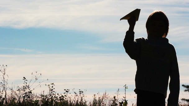Silhouette eines Jungen, der mit einem Papierflugzeug spielt. Einsamer Junge, der im Freien spielt.. - Filmmaterial, Video