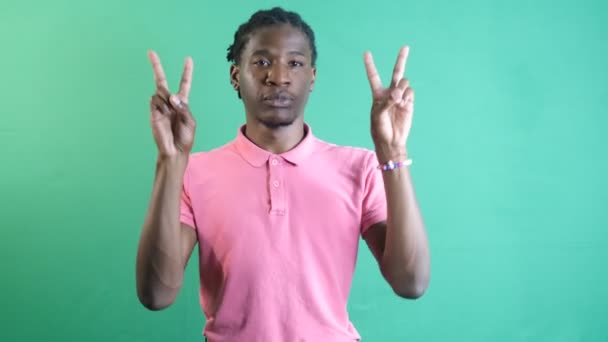 Молодий чоловік у рожевій футболці робить знак перемоги руками, чорна модель показує знак миру з пальцями, показує мову тіла та вирази обличчя перед зеленим екраном
 - Кадри, відео