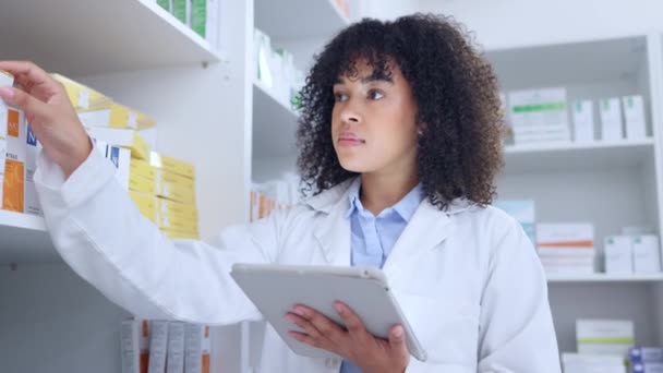 Pharmacist doing inventory with a digital tablet in a pharmacy. Young chemist with afro using pharma app to do stock update while counting and recording the quantity of medication in a drugstore. - Video, Çekim