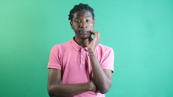 Image of black male thoughtfully putting his hand to his head, models solitary thinking gestures, image of emotions and facial expressions taken in front of the green curtain - Imágenes, Vídeo