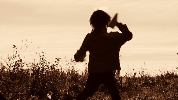 Silhouet van een jongen speelt met een papieren vliegtuigje. Eenzame jongen buiten spelen. Het kind begint vlak op een hemelachtergrond. Retro, zwart-wit, sepia. - Video