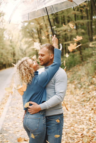 Man and woman kissing. Blonde curly woman and man standing in autumn forest and hugging. Couple wearing blue sweaters. - Foto, Imagem