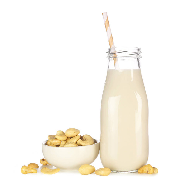 Cashew milk in a traditional bottle. Vegan, plant based, non dairy. Side view with ingredients isolated on a white background. - Photo, image