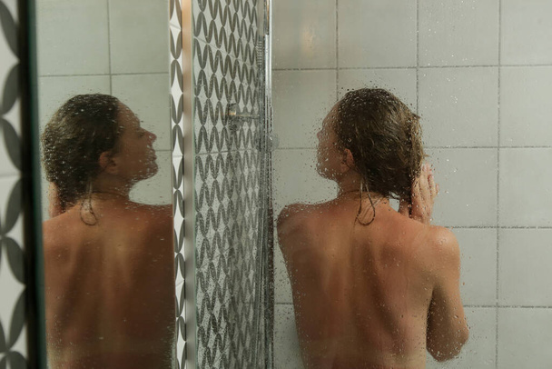 Nuori nainen suihkussa ja pesee hiuksensa suihkussa pukuhuoneessa. - Valokuva, kuva