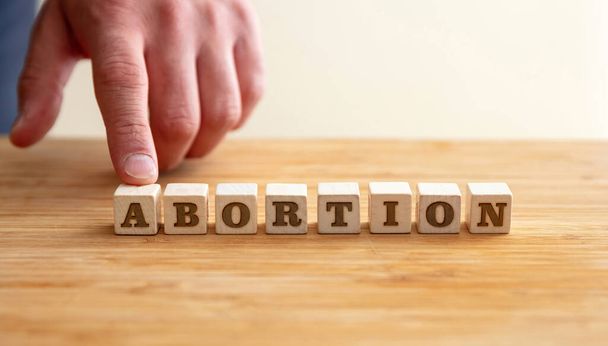 Abortion, Pregnancy termination concept. Male hand and Abortion Text on wooden blocks, copy space. - Photo, Image