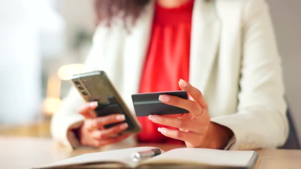 Closeup of womans hands holding a phone and credit card against blurry background with copy space. Young worker shopping online while sitting at a desk in a modern office. Lady making online booking. - Video