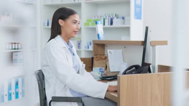 Young pharmacist working on computer at a pharmacy counter. Woman using technology to access drug database, does inventory checkup and dispensing online medicine prescriptions in a drugstore. - Materiał filmowy, wideo