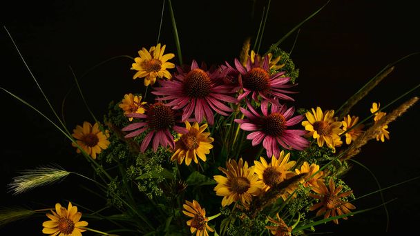 Een boeket bloemen verzameld in het wild in een eenvoudige glazen vaas geïsoleerd op een zwarte achtergrond. - Foto, afbeelding