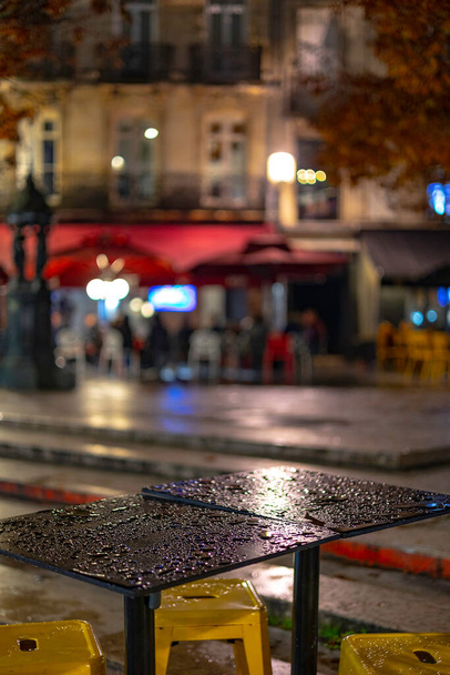 An empty outdoor area of a traditional french restaurant or cafe in a historic downtown. Tables and chairs without visitors.  Business in HoReCa. A rain droplets on table. - Foto, imagen