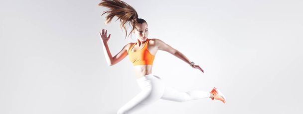 Confident young woman in sports clothing running against white background - Photo, image