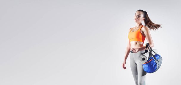 Attractive young woman in sports clothing carrying a bag against white background - Foto, imagen
