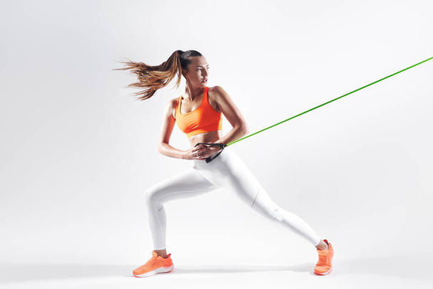 Confident young woman using resistance band while exercising against white background - Foto, immagini