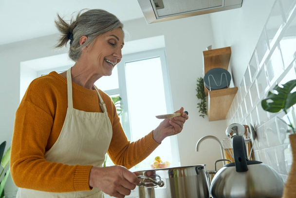 Elegant senior woman smiling while cooking at the domestic kitchen - Φωτογραφία, εικόνα