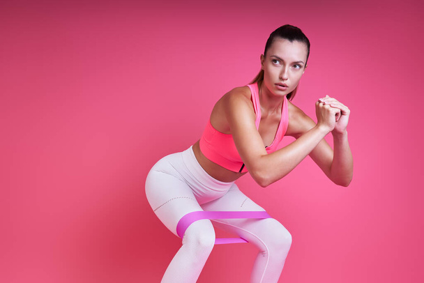 Confident young woman exercising with elastic band against pink background - Φωτογραφία, εικόνα