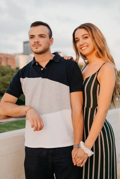 A couple of tourists are having fun with modern urban space in the background on a date at the sunset in Valencia. A girl is holding the hand of her boyfriend in the evening in Spain - Φωτογραφία, εικόνα
