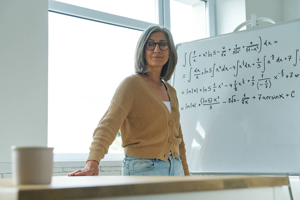 Senior woman teaching mathematics while standing near the whiteboard at classroom - Zdjęcie, obraz