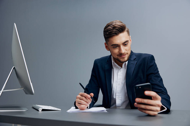 gutaussehender Geschäftsmann, der an einem Schreibtisch vor einem Computer sitzt, dessen Telefon isoliert ist. Hochwertiges Foto - Foto, Bild