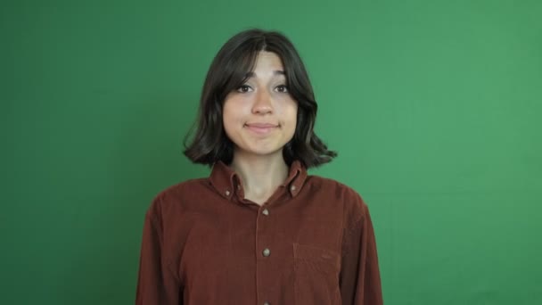 Beautiful girl with short hair making a bye-bye sign with her hand, see you body language, facial expression of young woman in front of green curtain - Video