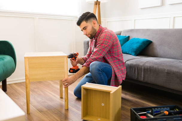 Attractive handy man drilling and using his tools while assembling night stand tables and doing home improvements  - Foto, Imagem