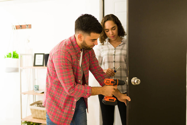 Handy young man and woman putting a new security doorknob with a drill on a door  - Foto, Bild