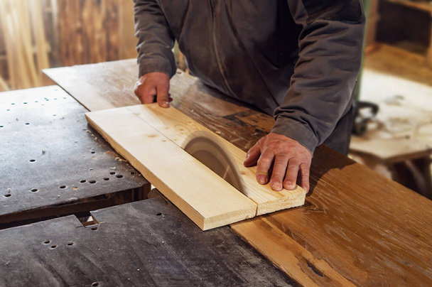 carpenter saws a wooden board with a carpentry machine.  old rustic carpentry shop. Working on woodworking machine - Foto, Imagen