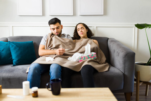 Sick caucasian couple covered with a blanket feeling bad and ill while recovering from the flu together on the sofa  - Foto, Bild