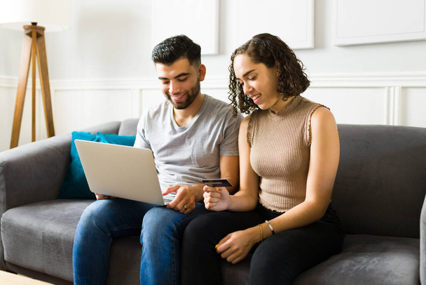 Happy woman and man smiling while doing online shopping on the laptop and paying with a credit card  - Zdjęcie, obraz