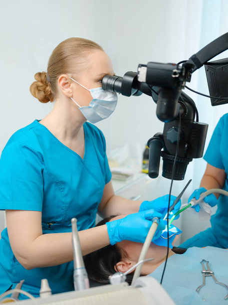 Female dentist using dental microscope treating patient teeth at dental clinic office. Medicine, dentistry and health care concept. Dental equipment - Photo, Image