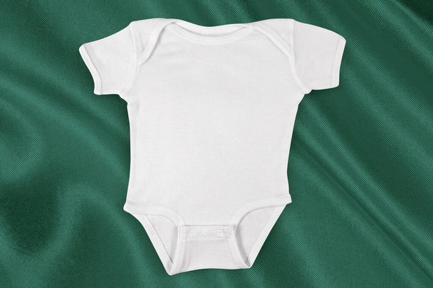 Top down view of a white onesie atop flowing green fabric. - Φωτογραφία, εικόνα