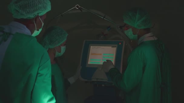 Kirurgi joukkue erikoiskokous ja keskustelu hoitoon potilaan leikkaus, kun käytät monitorin tietokoneen yhdessä leikkaussalissa sairaalassa, lääkärin keskustelu, lääketieteellinen käsite. - Materiaali, video