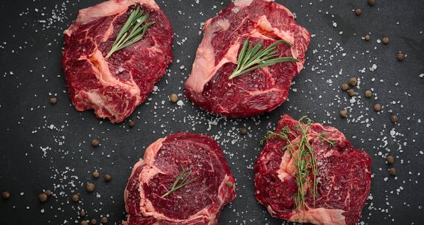 Nyers marhahús szűzpecsenye fekszik a vágódeszka és fűszerek főzés egy fekete asztalon, felülnézet - Fotó, kép