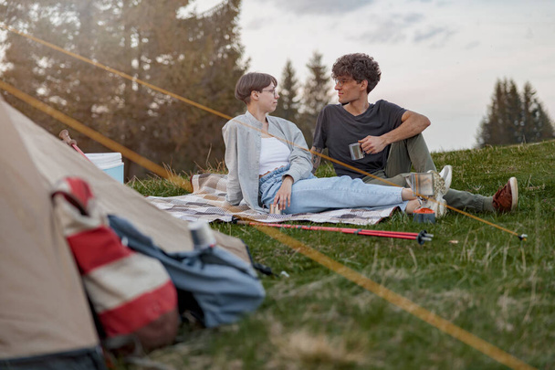 Fiatal fehér boldog férfi és nő ül a füvön a sátorban. Hegyi túra. Kiváló minőségű fénykép. - Fotó, kép