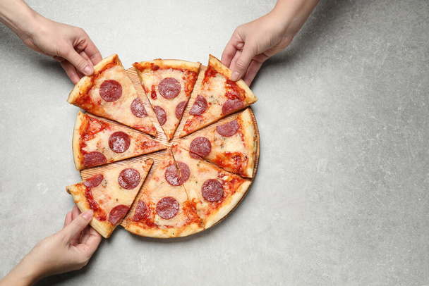 People taking slices of tasty pepperoni pizza at light grey table, top view - Foto, Imagem