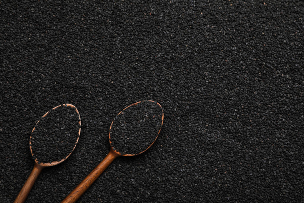 Wooden spoons on pile of black sesame seeds, flat lay. Space for text - 写真・画像