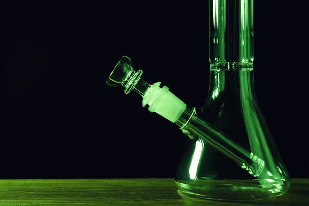 Glass bong on wooden table against black background, space for text. Smoking device - Foto, imagen