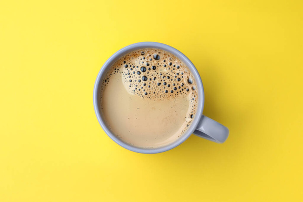 Grey mug of freshly brewed hot coffee on yellow background, top view - 写真・画像