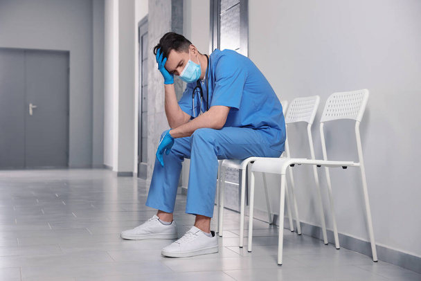 Exhausted doctor sitting on chair in hospital hallway - Fotoğraf, Görsel