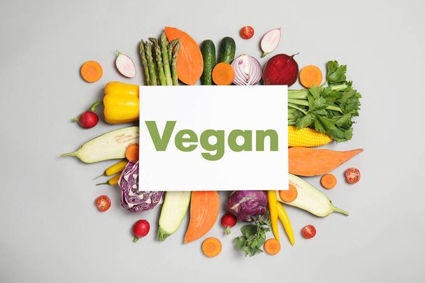 Paper card with word Vegan and fresh vegetables on white background, flat lay - Fotó, kép