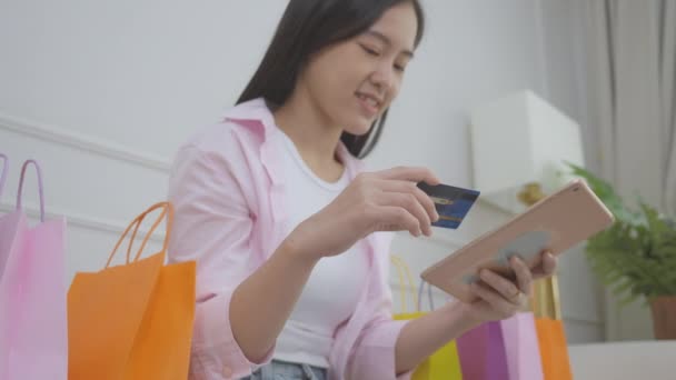 Mujer asiática joven sentada en el sofá usando la tableta digital de compras en línea con la compra de tarjetas de crédito a Internet, chica de la felicidad pagando con transacción financiera, compra y pago, concepto de negocio. - Metraje, vídeo