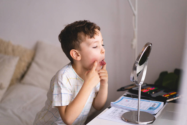 Konuşma terapisi konsepti. Sesi telaffuz eden şirin küçük çocuk aynaya bakıp dizüstü bilgisayarla konuşma terapisi dersi veriyor. - Fotoğraf, Görsel