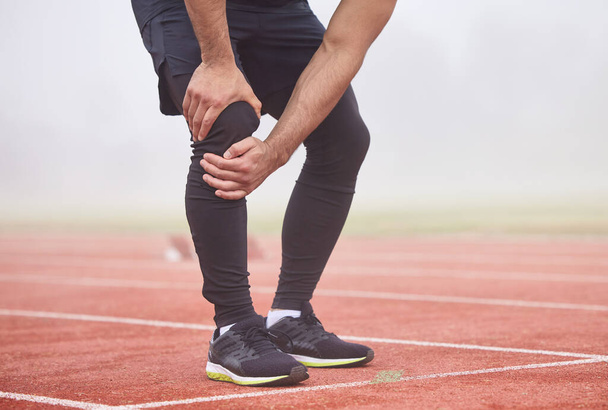 Looks like his race is run. an unrecognizable male athlete holding his knee in pain while standing out on the track - 写真・画像