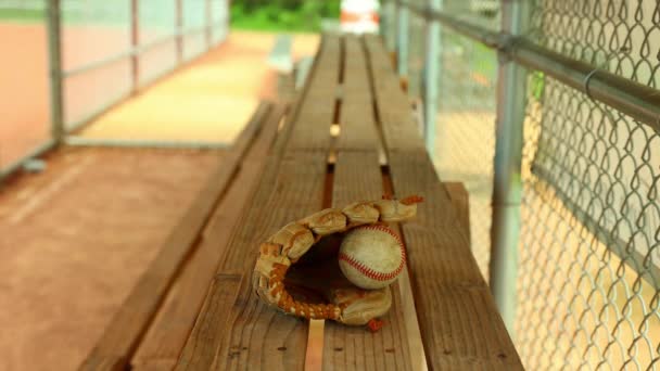 Youth baseball player picks up glove and ball off of team dugout bench - Filmagem, Vídeo