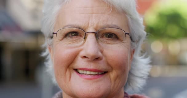Closeup of laughing senior woman thinking of a happy memory while standing alone in city. Portrait of smiling and content lady wearing optometry or optician prescription vision glasses to see in town. - Materiał filmowy, wideo